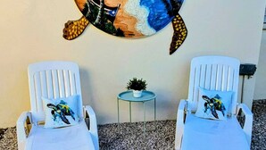 Un mural con temática de playa que muestra una tortuga y palmeras, dos sillas reclinables blancas y una mesa pequeña con una planta.