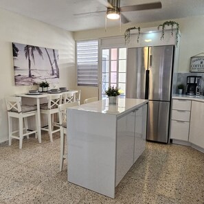 A modern kitchen with white cabinetry, a central island, and a stainless steel refrigerator.