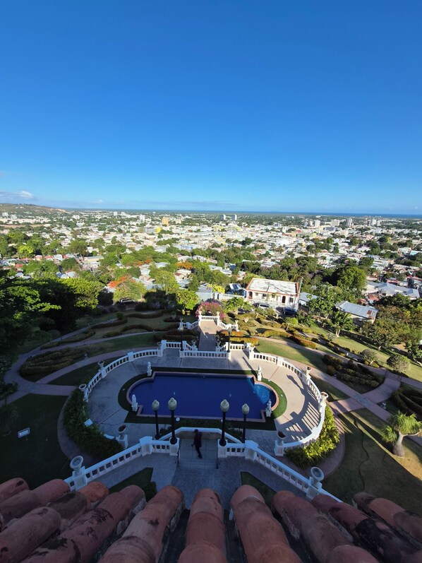 A view from a high vantage point overlooking a cityscape with a central circular pool area, surrounded by manicured gardens and pathways.