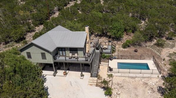 An aerial view of a house with a large deck, a swimming pool, and a stone staircase leading to the main entrance.