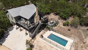 A modern two-story house with a pool, outdoor seating, and a staircase leading to a deck.