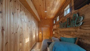 Ein Interieur einer Holzhütte mit einem Bett, einem Nachttisch und einem an der Wand befestigten Schild mit der Aufschrift 'Better Life'.