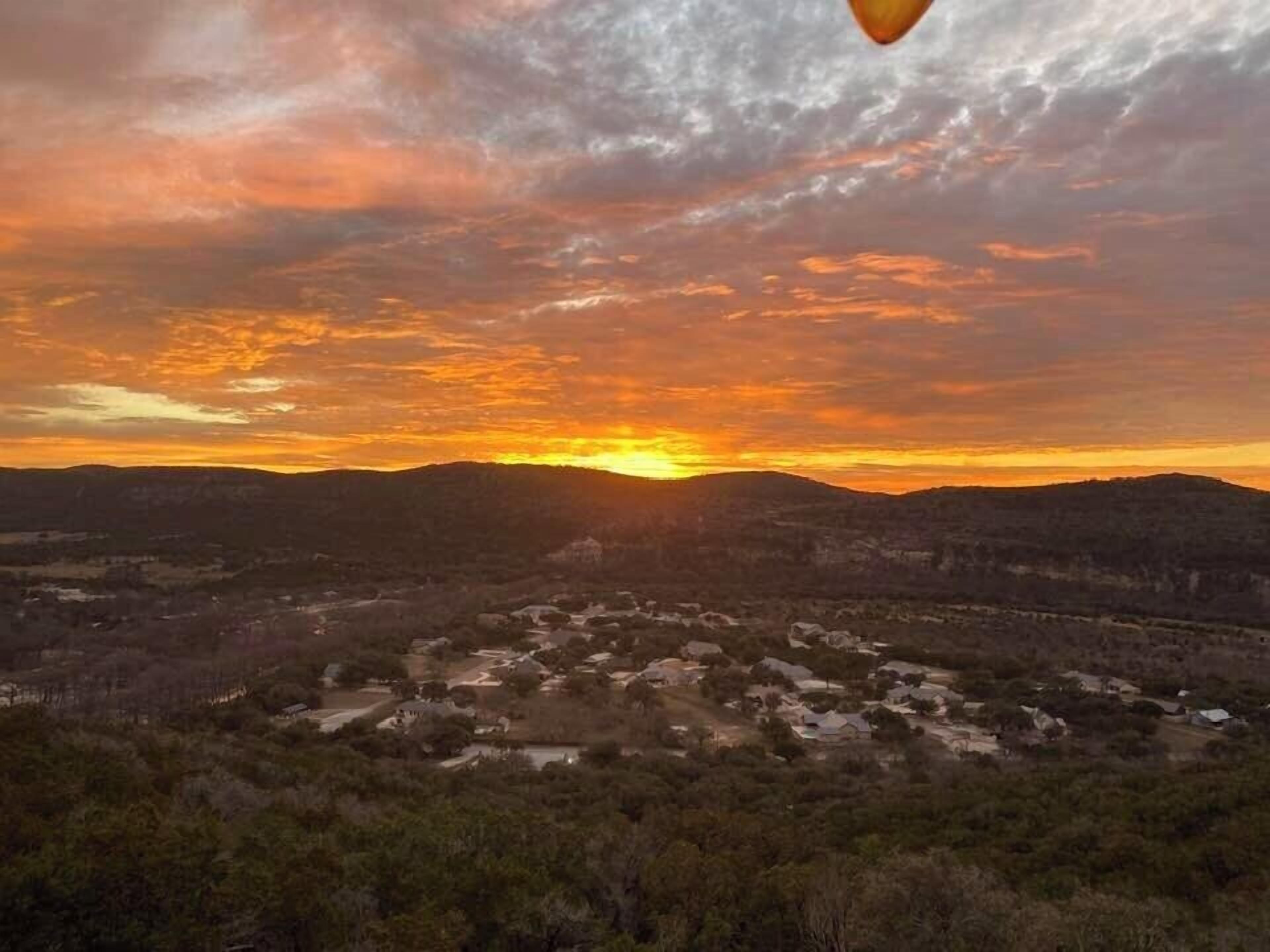 Et panoramaudsigt over en by i solnedgang med klar himmel og fjerne bjerge.