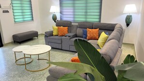 A living room with a grey sectional sofa, two side tables, a bench, and a large plant.