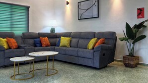A living room with a grey sectional sofa, two small round tables, a floor lamp, and a large potted plant.