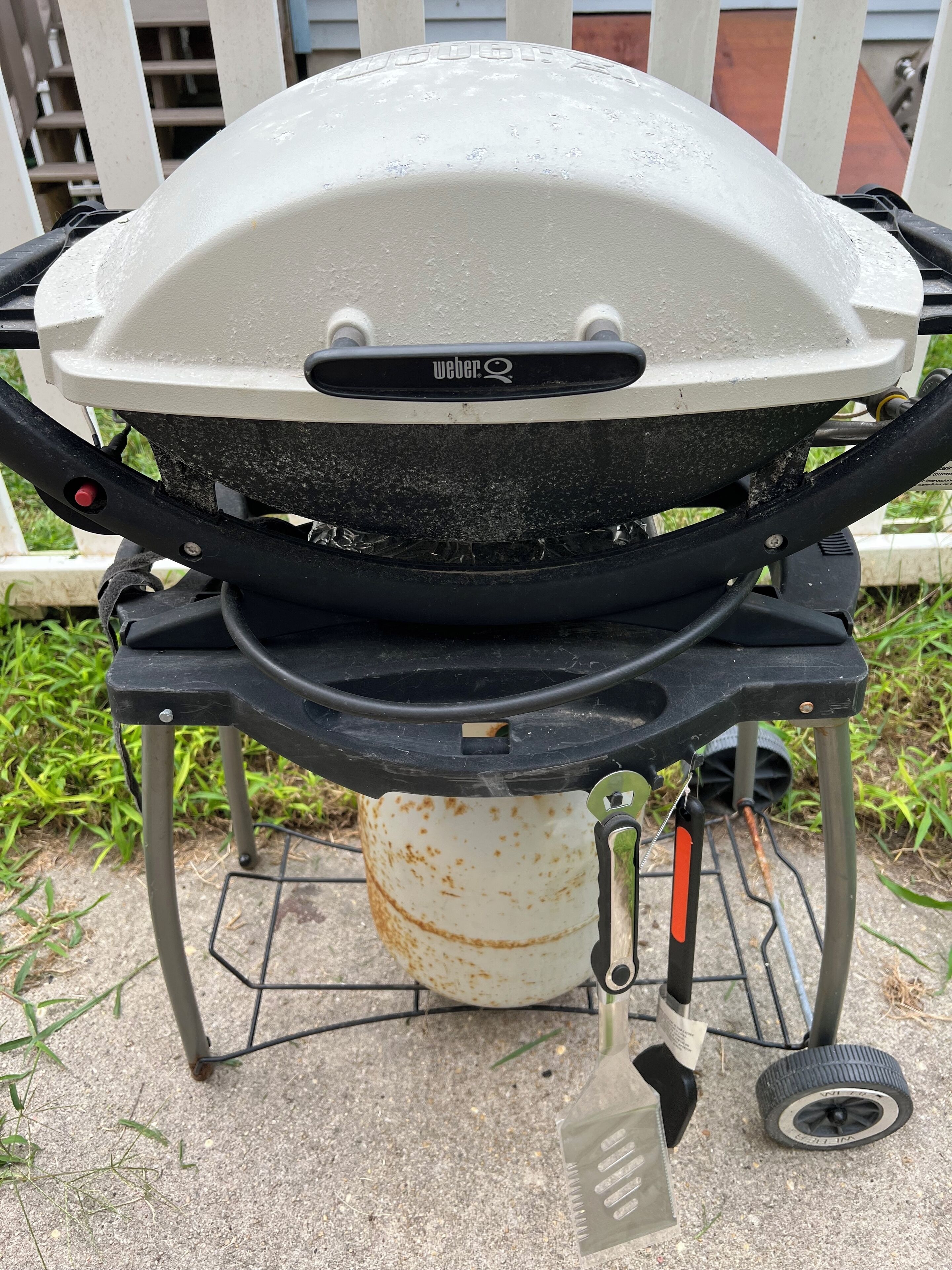 A portable Weber grill with a white lid, black handles, and a metal stand with wheels.