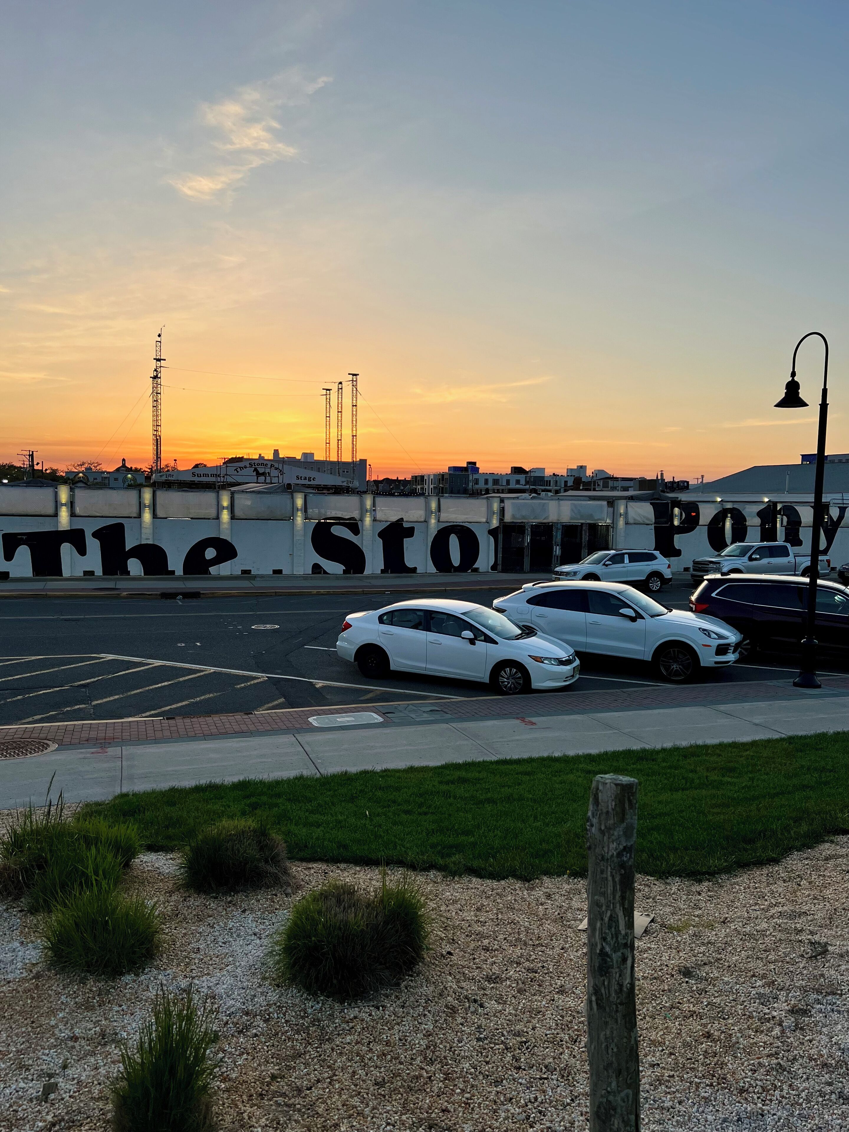 Een parkeerplaats met auto's, een gebouw met het bord 'The Stou' en een zonsondergang op de achtergrond.