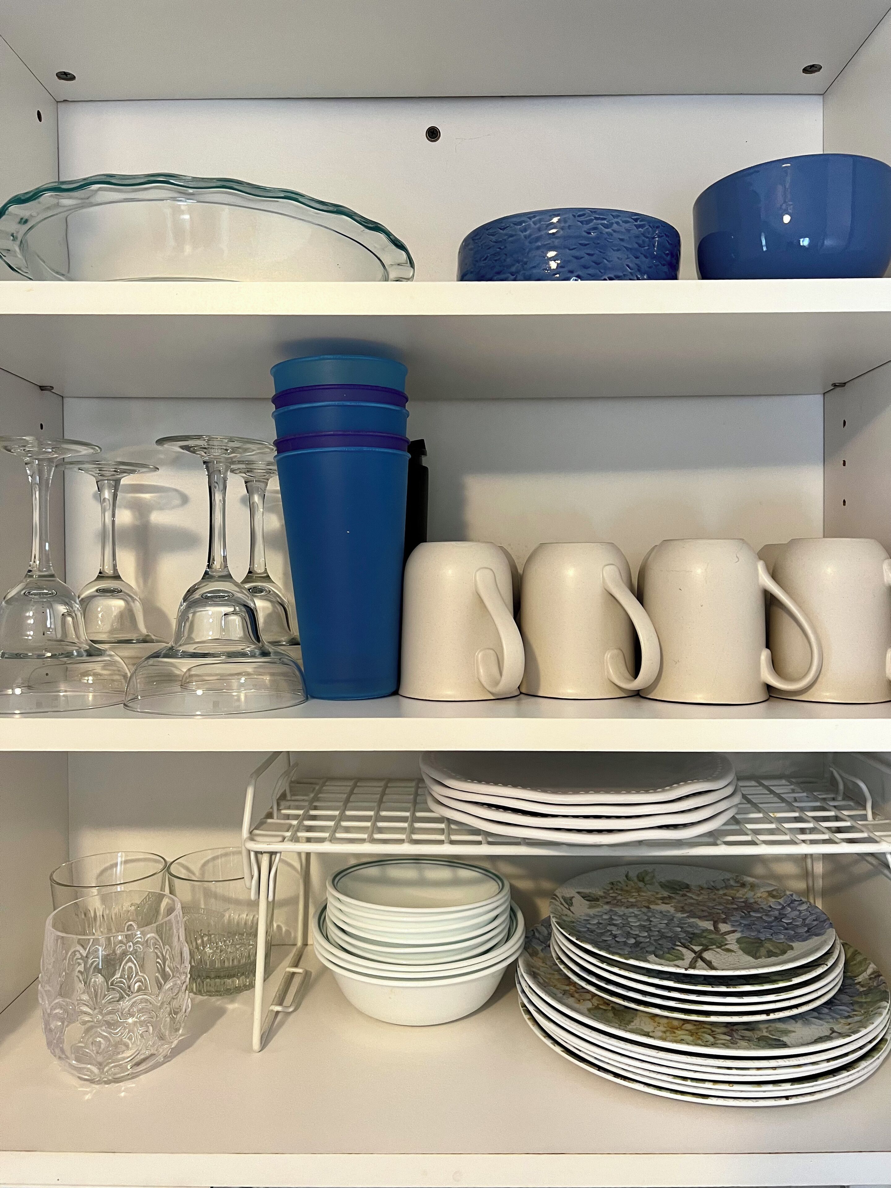 A kitchen shelf with glassware, mugs, and stacked plates.