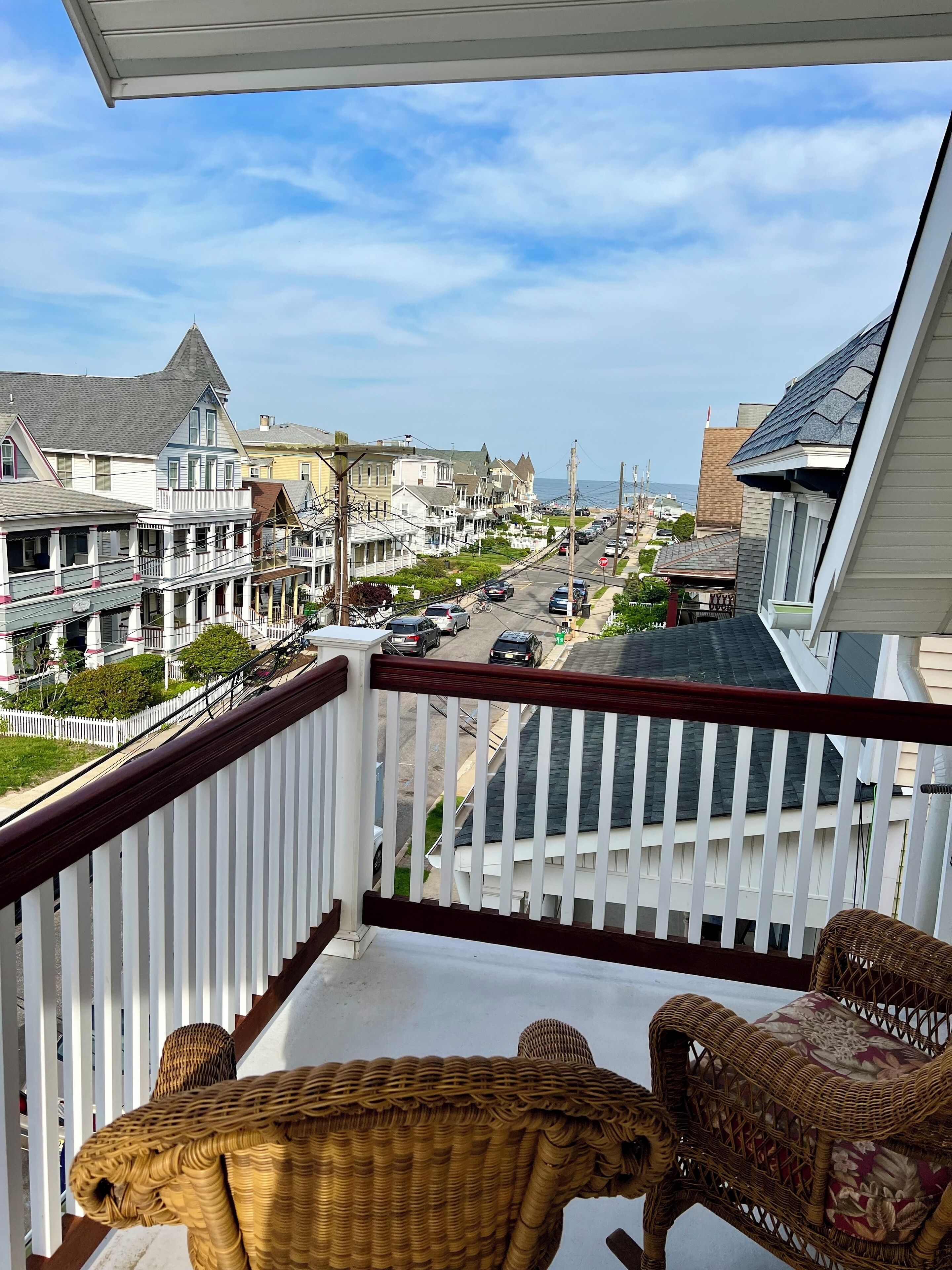 A balcony with wicker furniture overlooking a residential street with houses and a clear sky.