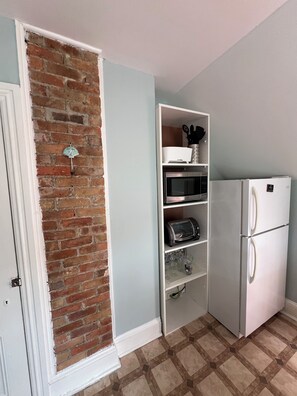 A kitchen with a brick wall, white cabinetry, a white refrigerator, and a microwave.