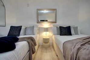 A hotel room with two beds, a bedside table with a lamp, a mirror on the wall, and a wooden floor. - Central Versatile Studio (Portsmouth)