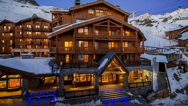 Eine mehrstöckige Holzhütte mit Balkonen, einem Steineingang und einem Schild mit der Aufschrift 'CHALET VAL2400'.