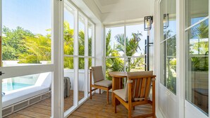 A sunroom with a wooden deck, a pool, and large windows offering a view of palm trees.