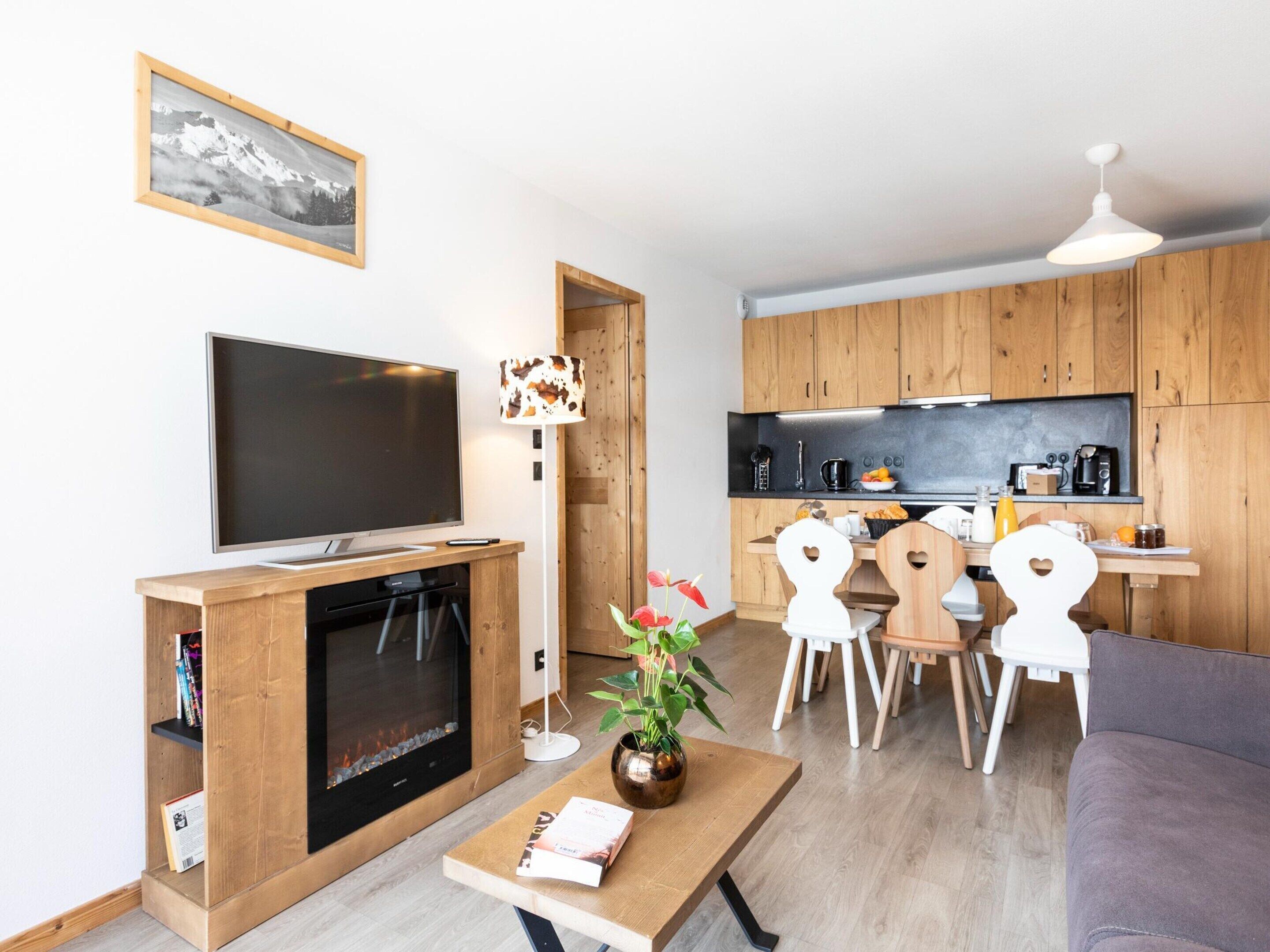A modern living room with a flat-screen TV, fireplace, wooden furniture, and a dining area with a table and chairs.