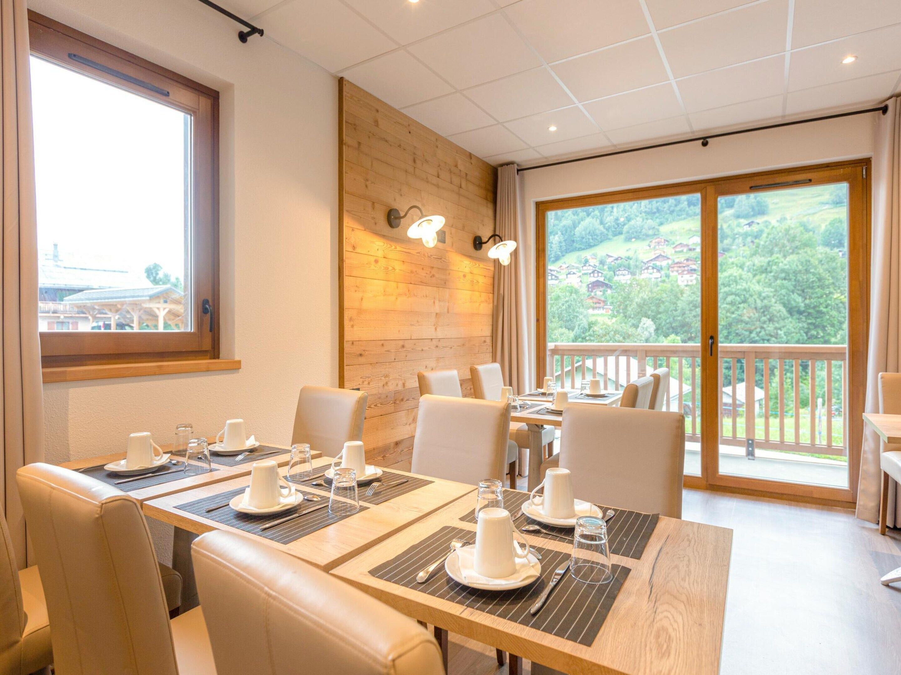 A dining area with tables set for four, wooden walls, and large windows offering a view of a green landscape.