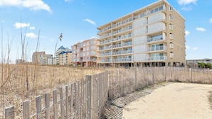 Un hotel de varios pisos con balcones, un sendero de arena y una valla de madera.