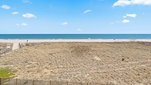 Una playa con un sendero arenoso que lleva al agua, una cerca de madera y un cielo azul despejado.