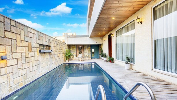 A modern pool area with a stone wall, wooden deck, and a clear blue pool. - Mordern Rooftop Restro and Pool at Udaipur (Udaipur)