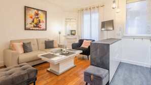 A modern living room with a sofa, armchair, and ottoman, a fireplace, and a TV. - Charming Apartment - 2br/4p- Javel (Paris)