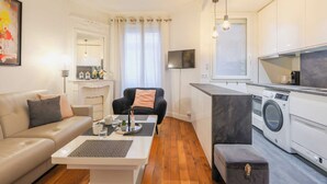 A modern living room with a sofa, coffee table, and a chair. There is a kitchen area with a washing machine and a TV. - Charming Apartment - 2br/4p- Javel (Paris)