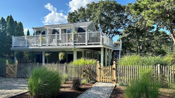 A two-story house with a balcony, surrounded by a wooden fence and various plants.