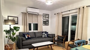 A living room with a grey sofa, a wooden chair, a small table, and a potted plant.