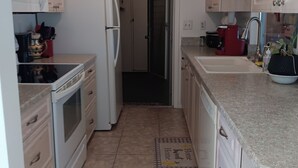 Cocina compacta con armarios blancos, microondas, refrigerador, estufa y pileta.