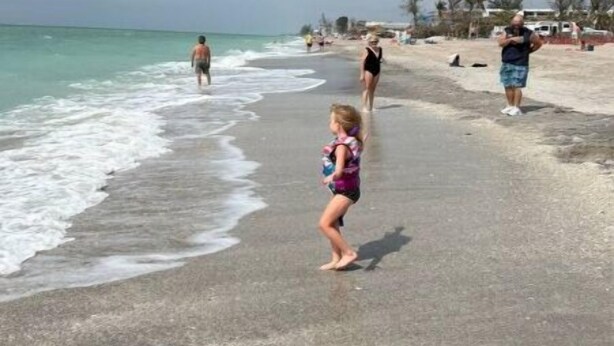 Una playa con gente caminando, cielo despejado y mar tranquilo.