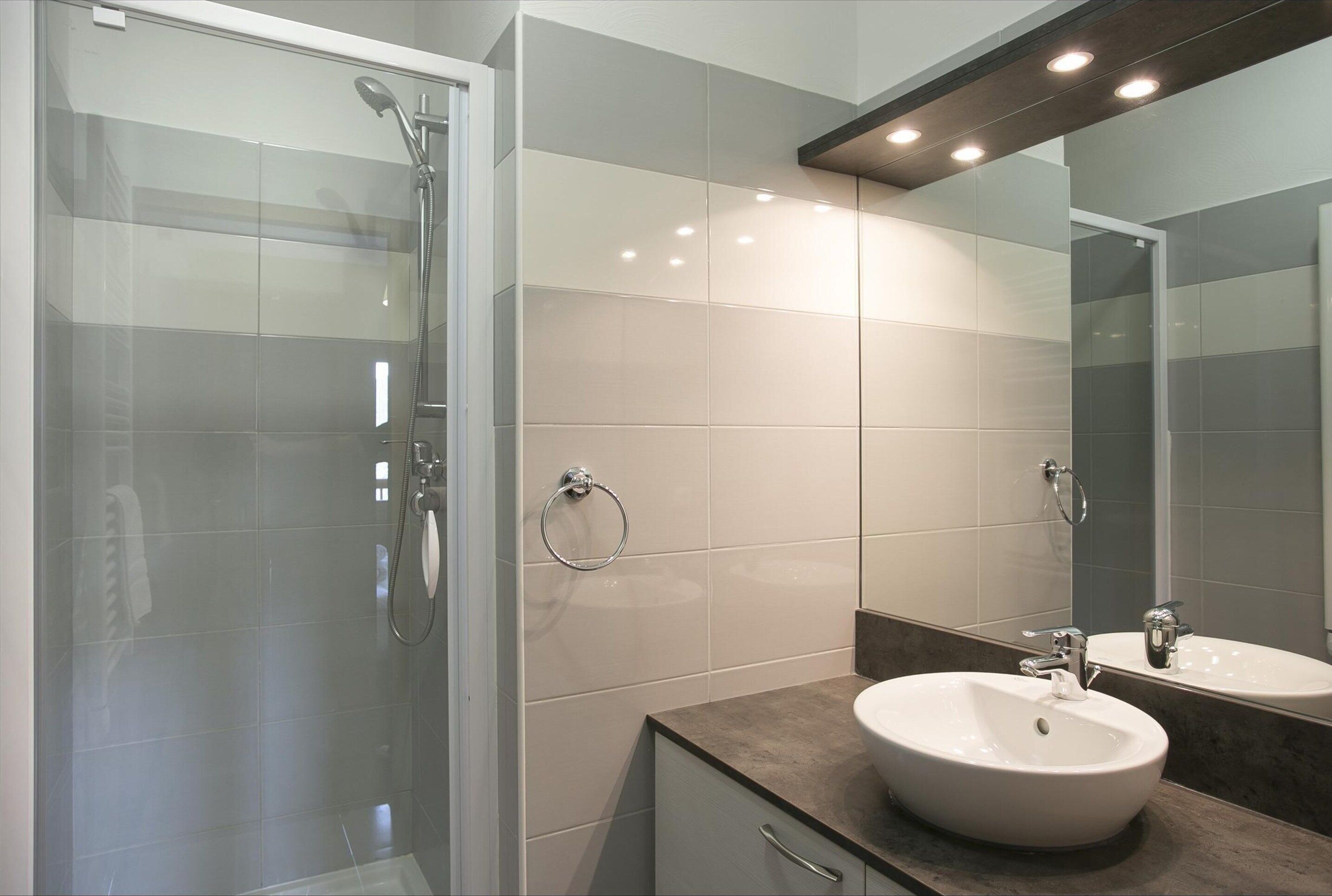 Une salle de bain moderne avec une douche à l’italienne en verre, un lavabo blanc et un grand miroir.