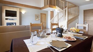 A dining area with a table set for a meal, wooden chairs, a staircase, and a television mounted on the wall. - Apartment in Sainte-foy With Ski-in/ski-out (Sainte-Foy-Tarentaise)
