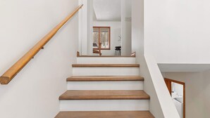 A staircase with wooden steps and a wooden handrail leading to a room with a window and a chair. - Scenic Escape Kayaks Game Room on M22 (Frankfort)