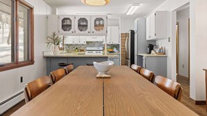 A modern kitchen with white cabinets, a wooden dining table, and a large window. - Scenic Escape Kayaks Game Room on M22 (Frankfort)