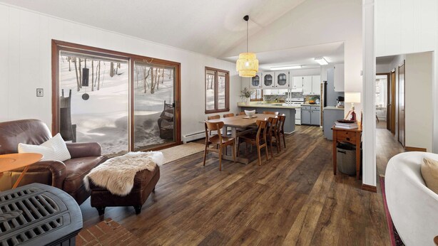 A spacious living room with a fireplace, a dining area with wooden furniture, and a kitchen in the background. - Scenic Escape Kayaks Game Room on M22 (Frankfort)