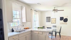 A kitchen with white cabinets, a sink, and a dining area with a table and chairs. - Charming & Spacious 4 BR w/ Private Backyard in lovely Summerville (Summerville)