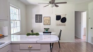 A modern kitchen with a white island, black chairs, and a ceiling fan. - Charming & Spacious 4 BR w/ Private Backyard in lovely Summerville (Summerville)