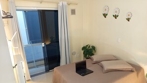 A bedroom with a bed, a laptop, a potted plant, and a sliding glass door leading to a balcony. - Apto 102 Ed Gabriel na divisa do Parque (Piratuba)