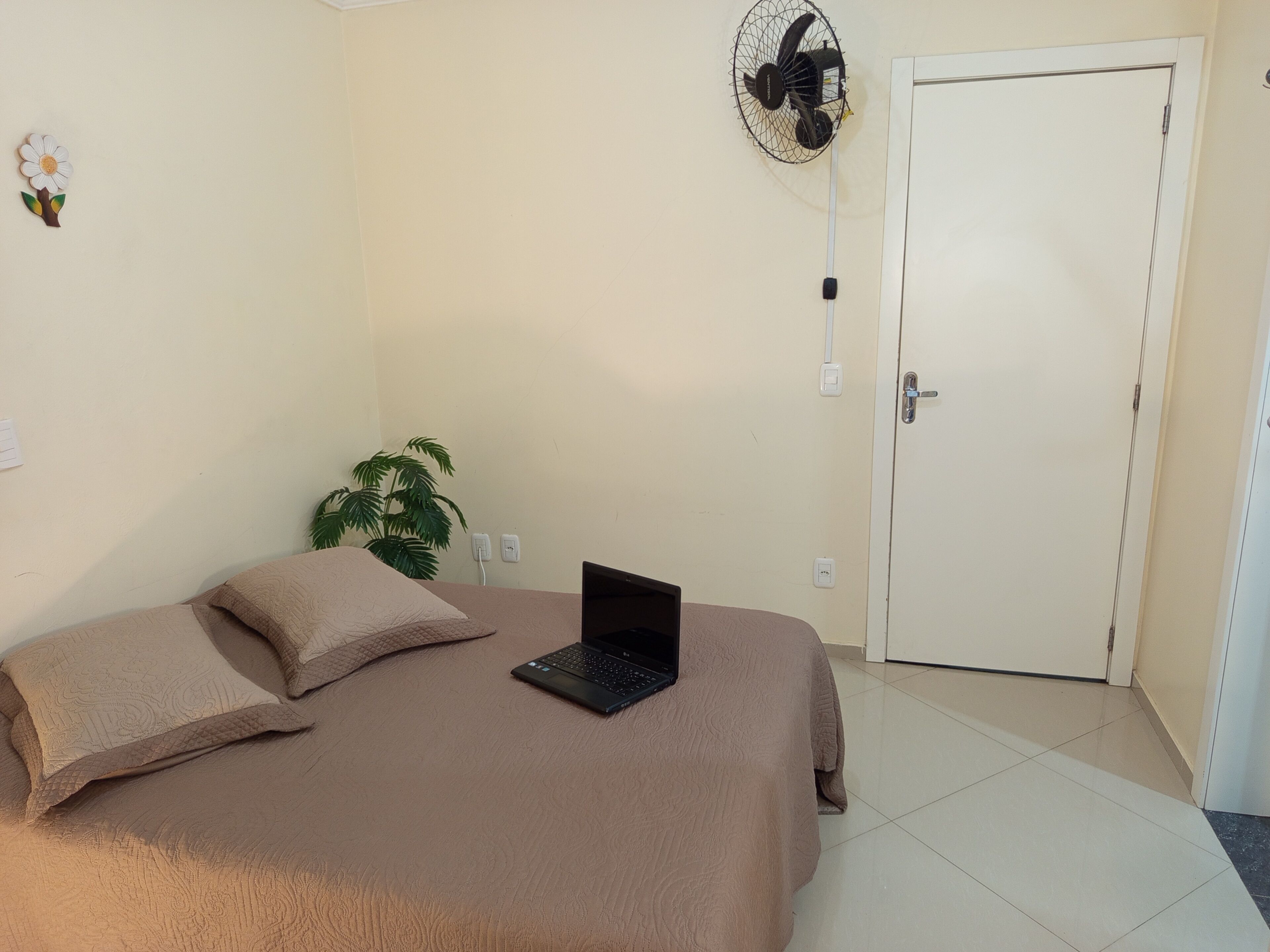A bedroom with a bed, a laptop, a fan, and a door.