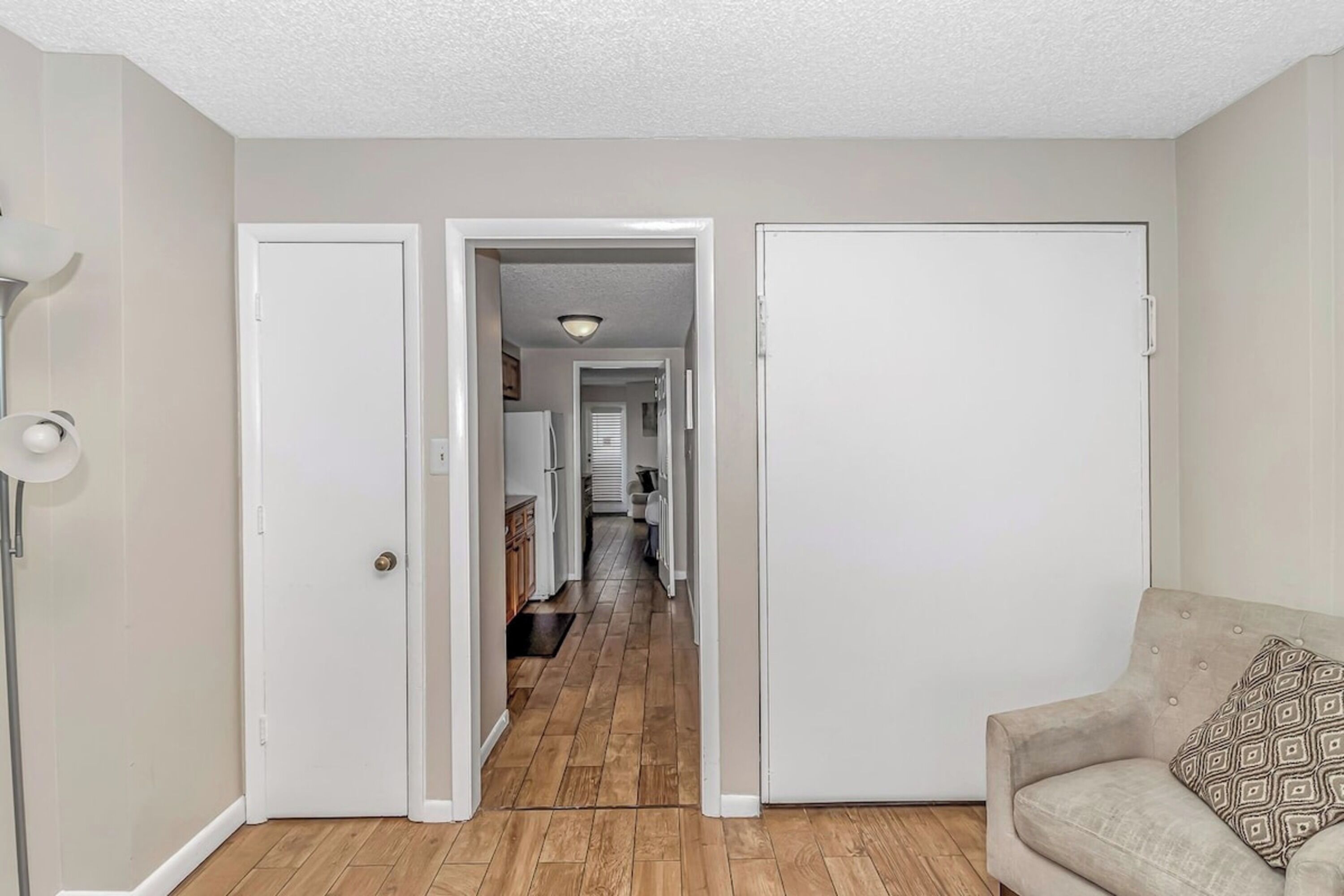 A hallway with a wooden floor, white walls, and a beige sofa with a patterned pillow.