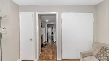 A hallway with a wooden floor, white walls, and a beige sofa with a patterned pillow.