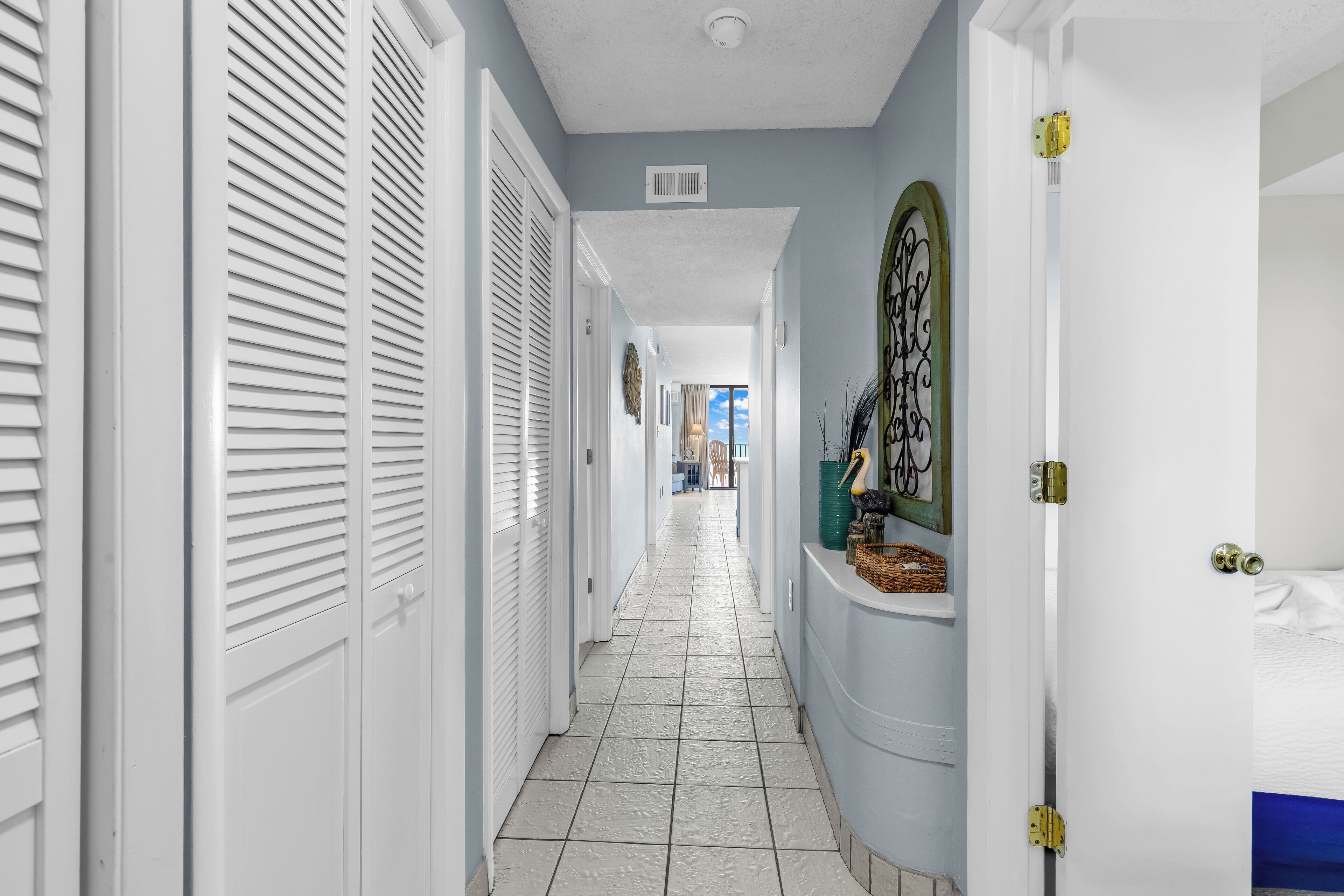 A hallway with white doors, a tiled floor, and a view into another room.
