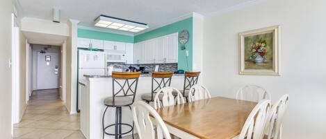 Une cuisine avec des meubles blancs, un îlot central doté de tabourets et une table à manger avec des chaises.