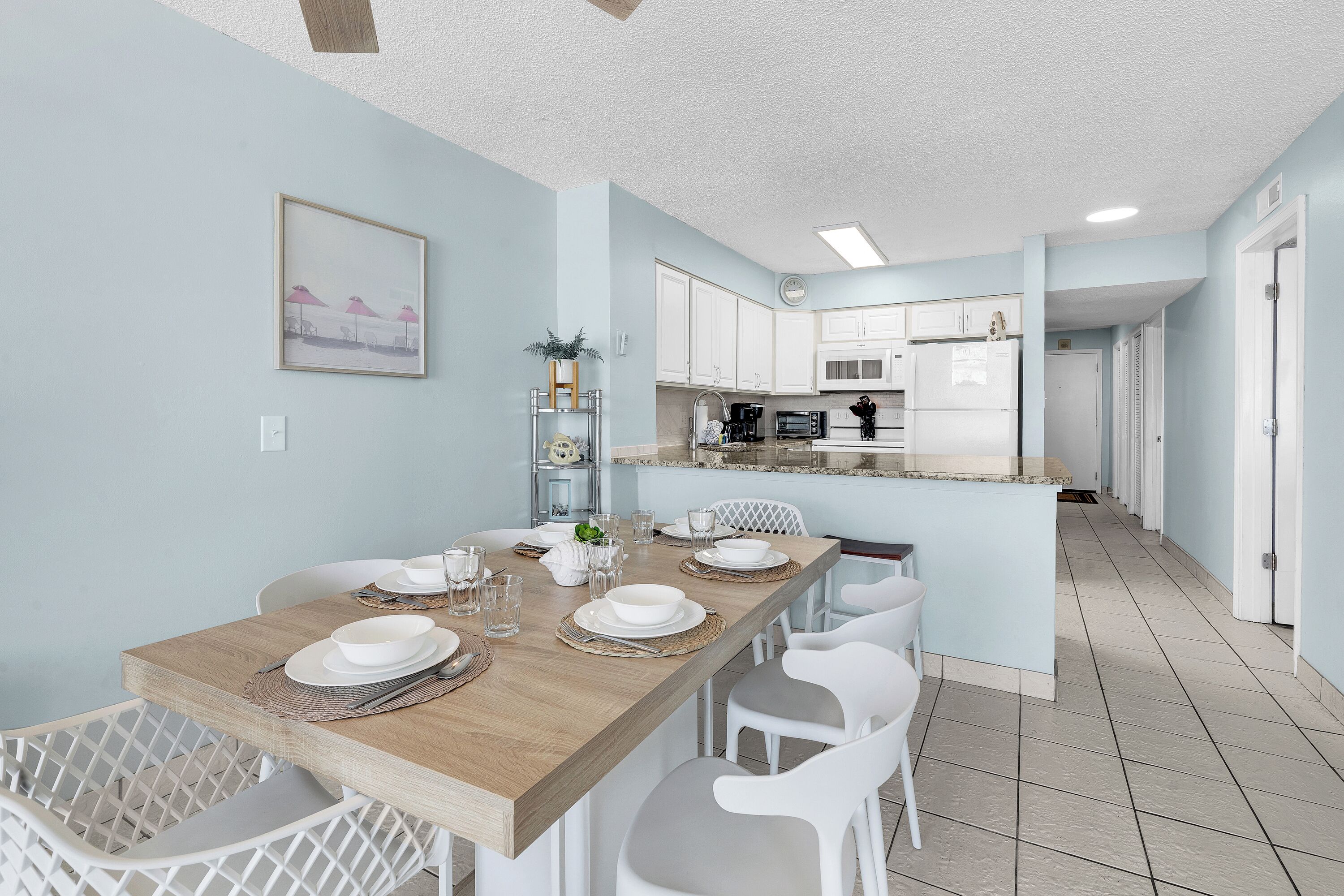 A modern kitchen with white cabinets, a wooden dining table, and white chairs.