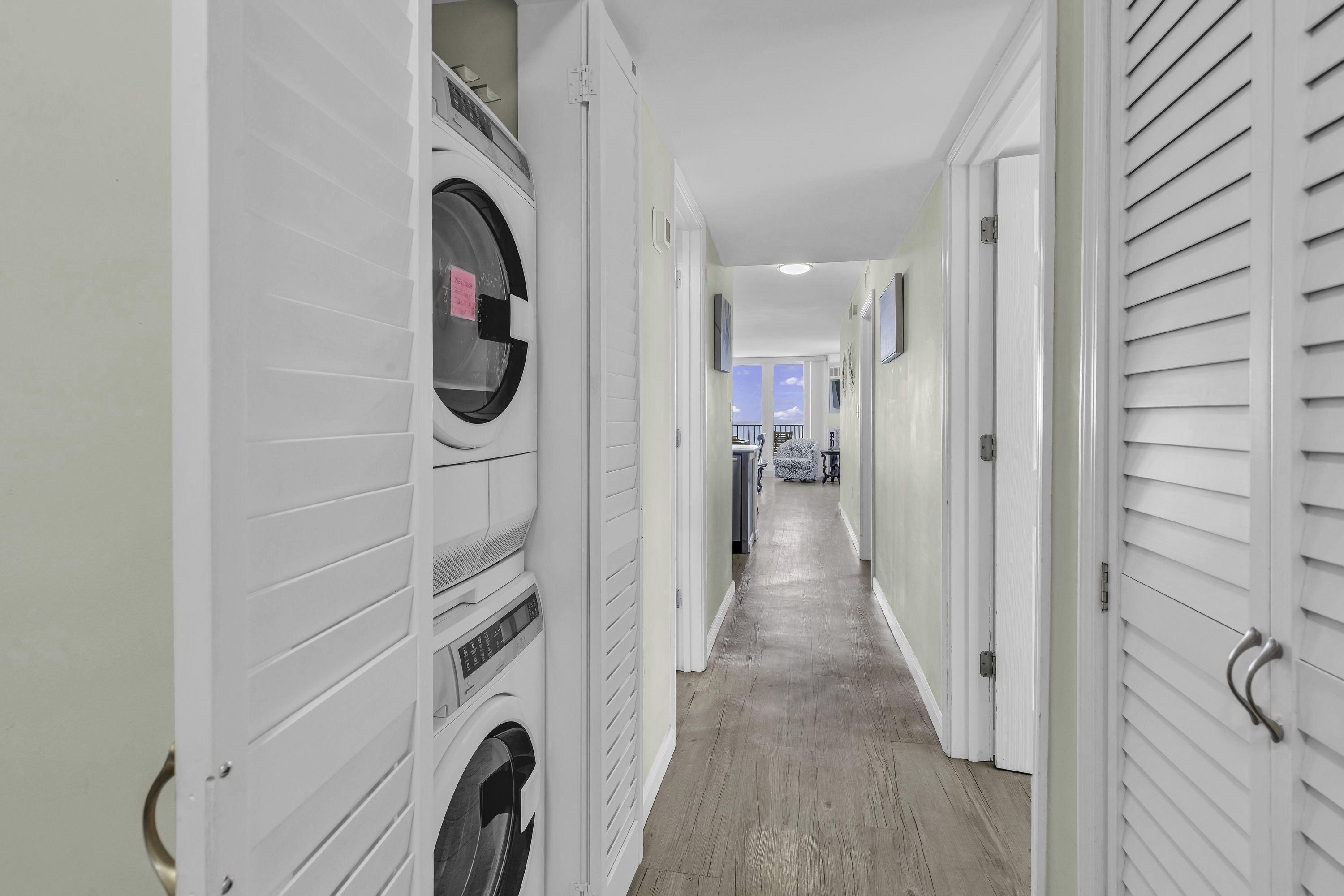 Une buanderie équipée de plusieurs lave-linge et sèche-linge, un couloir menant à un balcon et une porte dotée d’une poignée.