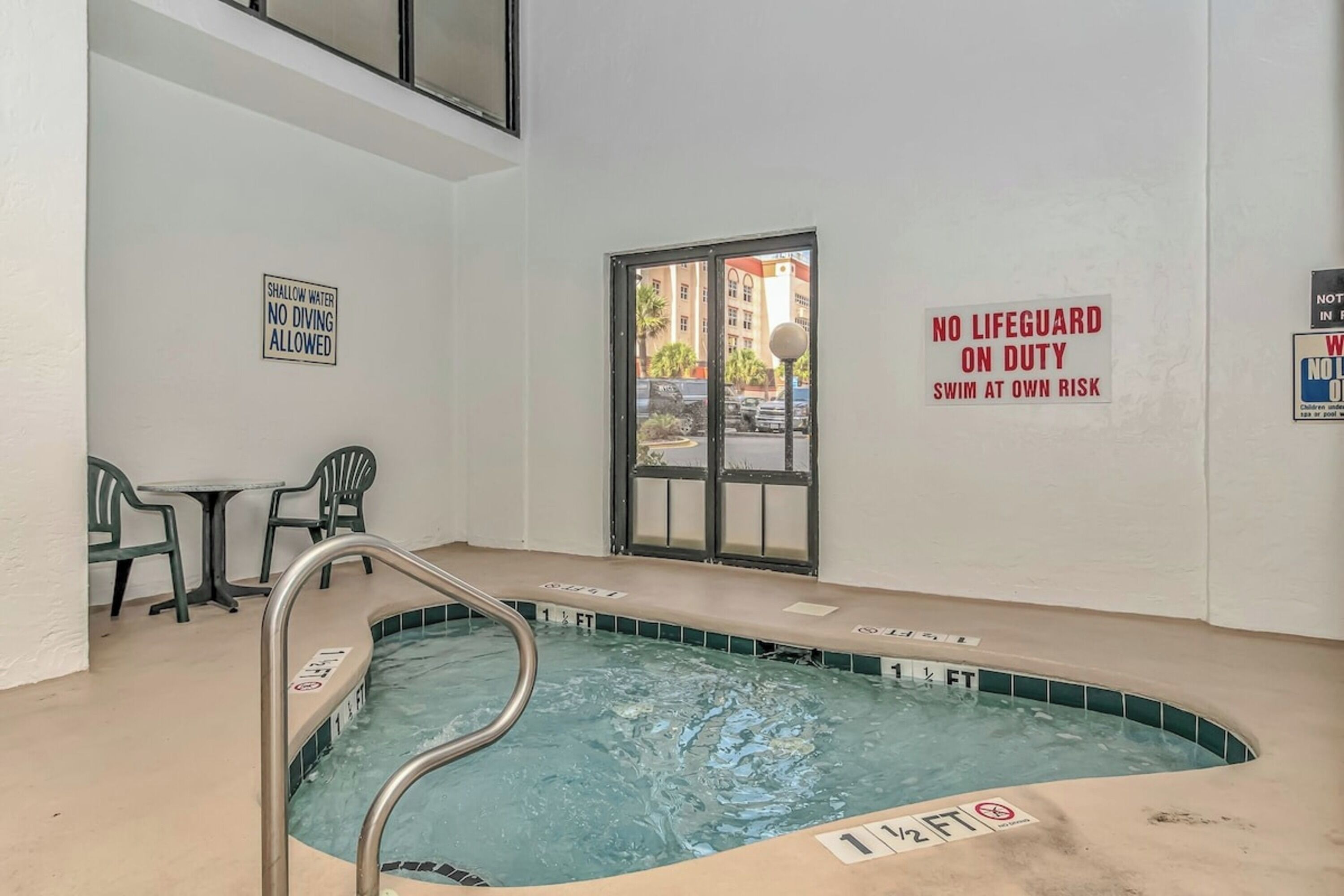 An indoor swimming pool with shallow water, a lifeguard on duty sign, and a no diving allowed sign.