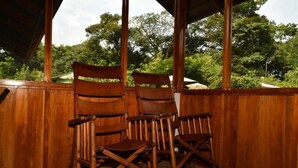 A wooden rocking chair in a covered outdoor area with a stone floor and a view of lush greenery. - Hacienda Barú Lodge (Savegre)