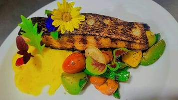 Un plato con pescado a la parrilla, verduras asadas y salsa amarilla.