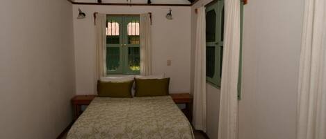 Un dormitorio con cama, ventilador de techo, ventana con cortinas y una puerta.