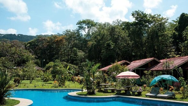 A pool surrounded by lush greenery and a few buildings with red roofs. - Hacienda Barú Lodge (Savegre)