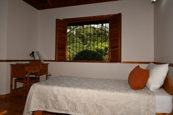 Een slaapkamer met een bed, een bureau en een raam met uitzicht op groen.