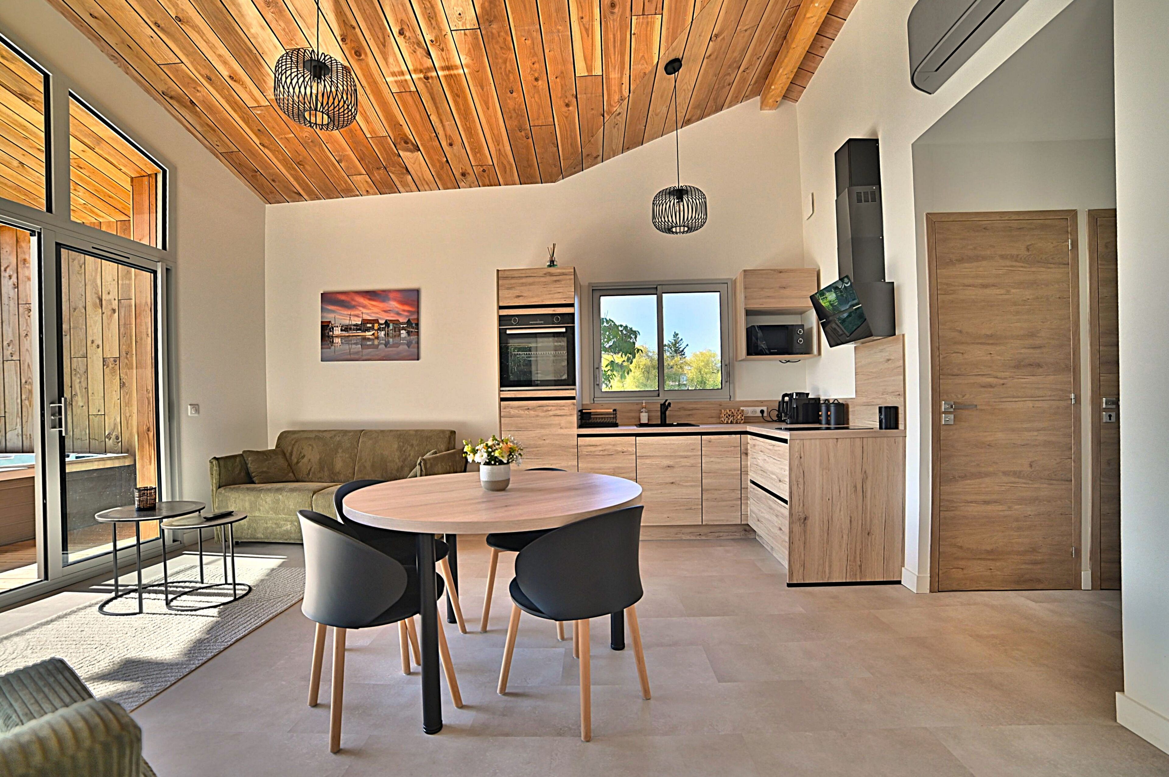 Una cocina moderna con armarios de madera, un comedor con una mesa redonda y sillas, y un ventanal que proporciona luz natural.